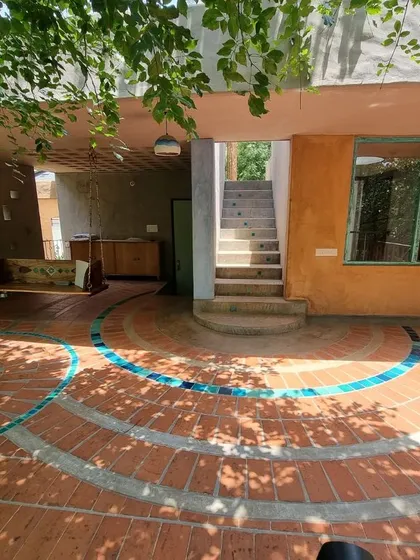 The morning terrace is an extension of the living space, with a floor pattern of terracotta and blue tiles that flows from inside to out. It is a space designed for slow mornings, shaded by the leaves of the surrounding trees.