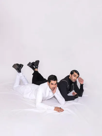 A creative composition featuring two models in contrasting black and white suits. The overhead shot and relaxed poses create a visually interesting editorial image that showcases both outfits.