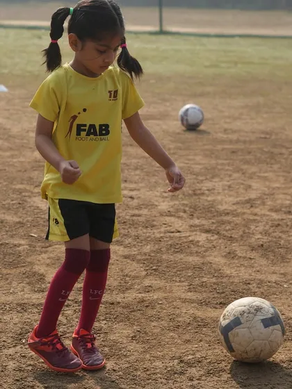 A young player with pigtails stands over the ball. The football field is a classroom, and every session is a lesson in teamwork, perseverance, and strategic thinking.
