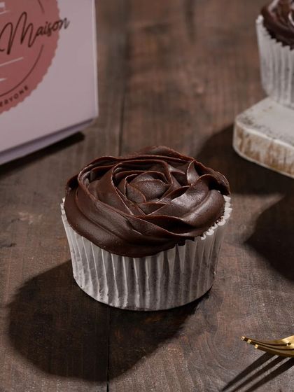 A chocolate cupcake with a beautiful frosting rose, shot with moody lighting. This elegant shot is perfect for showcasing cake decorating skills.