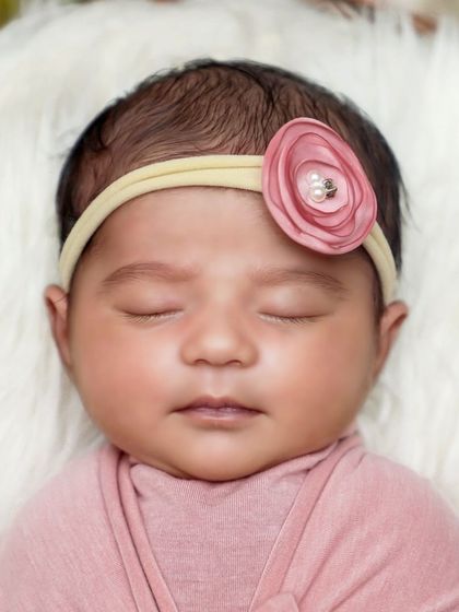 A beautiful close-up of a newborn's face, highlighting her delicate features and the soft texture of the pink wrap and floral headband.