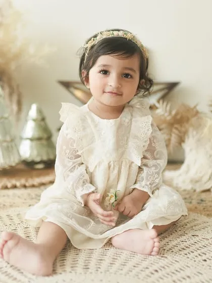 A one-year wonder. This beautiful little girl in a lace dress is the picture of innocence for her first birthday milestone portrait, set against a neutral, boho-inspired backdrop.