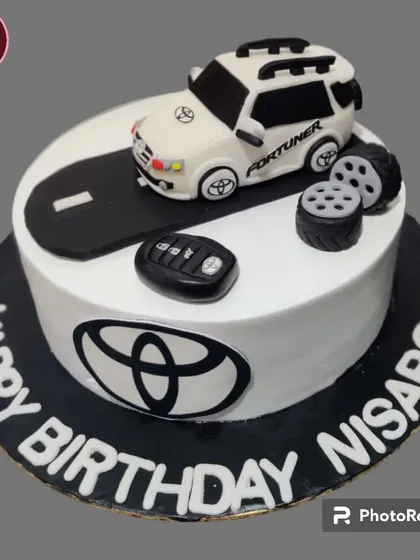 A cool Toyota Fortuner-themed cake for a car lover. The design features the yin-yang symbol, the Toyota logo, and a detailed car topper with keys.