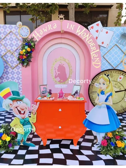 A cake and gift table setup with the Mad Hatter and Alice cutouts.