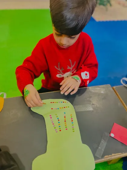This boy is meticulously placing dots on his stocking craft, showing great focus.