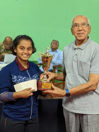 Harshika K proudly receives her trophy. This moment captures the culmination of her hard work, leading to her victory in the under 15 and under 17 girls' singles events.