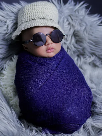 A close-up of our little "boss baby," showing the details of the knitted hat and cool round sunglasses on a swaddled newborn.