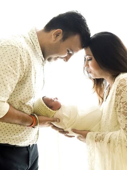 An intimate family portrait with a newborn, using soft backlighting to create a dreamy, high-key effect. The parents' connection as they hold their baby is the heart of this image.