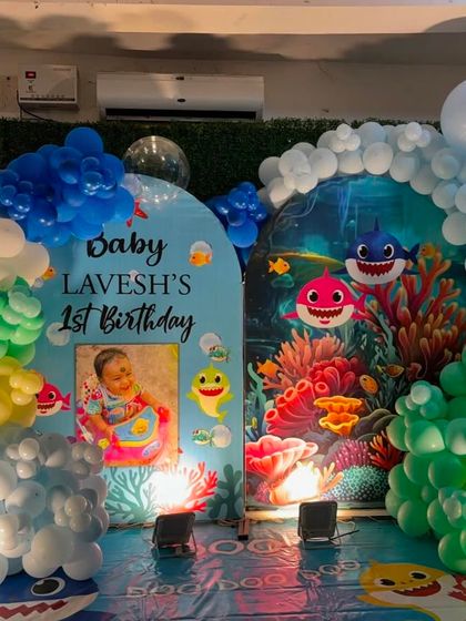 A vibrant Baby Shark themed setup against a green hedge wall. This decoration uses colorful backdrops and balloon arrangements to create an underwater scene.