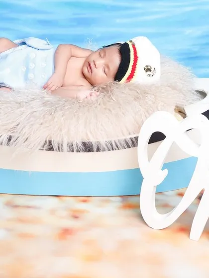 A one-month milestone photo with a nautical theme, featuring the baby sleeping in a boat prop with a "One" sign.