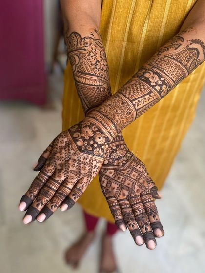 This design demonstrates how beautifully intricate henna looks against a vibrant outfit. The dark lines of the jaal work and floral bands stand out, covering the arms completely.