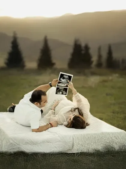 Sharing the first glimpse of their baby in a dreamlike setting. The couple looks at the sonogram together while lying on a bed in an open field, a unique and creative concept.