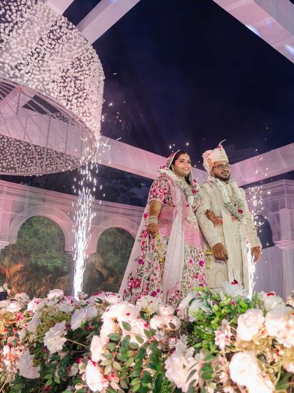 A joyous moment for the couple, surrounded by a sea of white flowers and celebratory sparklers. The image captures the magical atmosphere created by the thoughtful lighting and decor.
