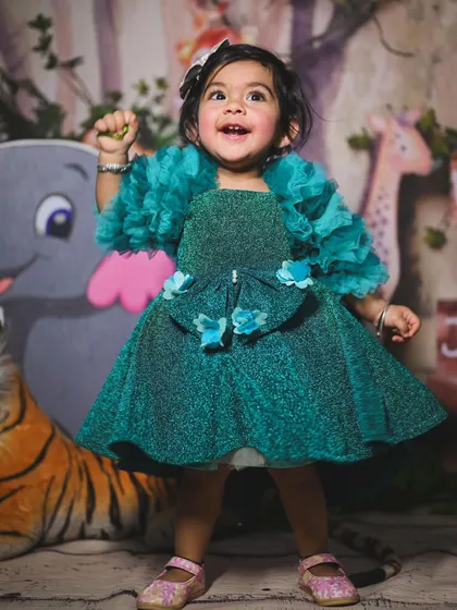 A full-length shot of the birthday girl in a beautiful dress, standing in front of the jungle backdrop. The decor is designed to complement the child's outfit and the party's color scheme.