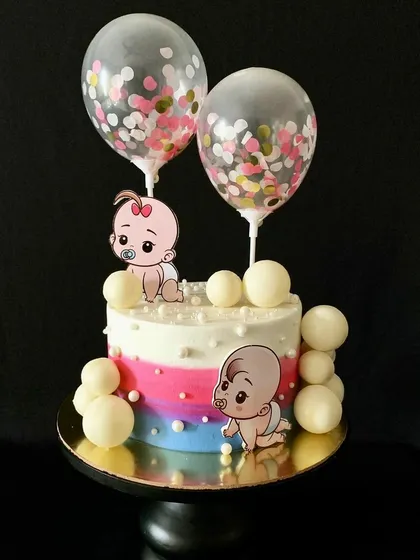A custom gender reveal cake with pink and blue ombre, cute baby toppers, and confetti balloon toppers.