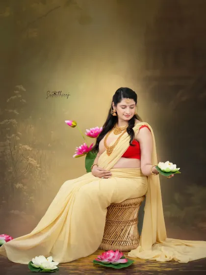 A beautiful portrait of a mother-to-be in a flowing yellow saree, surrounded by lotus flowers. The setup creates a divine and serene atmosphere, celebrating the goddess within.