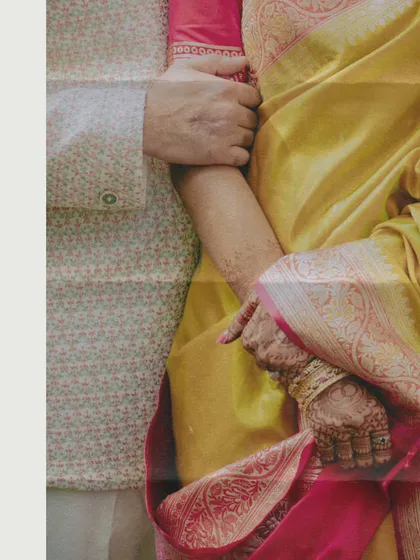 A close-up, artistic shot focusing on the texture and colors of the couple's traditional attire and the bride's mehndi.