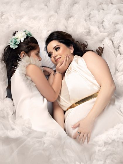 A truly angelic moment between mother and daughter, lying together on a bed of white ruffles. This overhead shot captures their loving bond in a beautiful and artistic way.