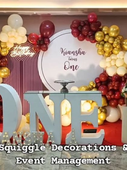 A rustic and charming first birthday setup with a teddy bear, wooden fence props, and a large light-up "ONE".