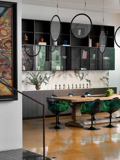 The dining room in this Bengaluru home by Keystone Studio is a dramatic space, featuring emerald green chairs, a book-matched marble wall, and sculptural pendant lights.