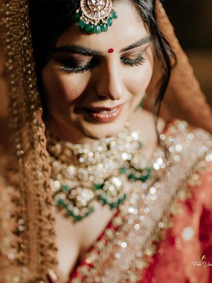 A soft, beautiful close-up of the bride, her eyes closed, highlighting her flawless makeup and stunning emerald necklace.