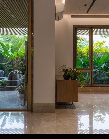 A view from an interior space looking out onto a covered patio. The reflection in the polished marble floor mirrors the garden, further enhancing the connection between the indoor and outdoor environments.