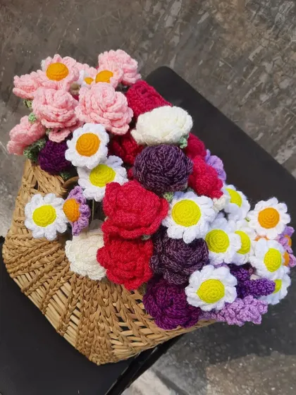 A traditional wicker basket filled with a colorful assortment of handmade crochet flowers. This shows how they can be displayed in a shop or used as a beautiful, permanent floral arrangement.