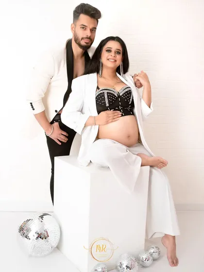 A confident and stylish portrait of an expecting couple. They pose in modern black and white outfits, looking directly at the camera with a cool, fashionable energy.