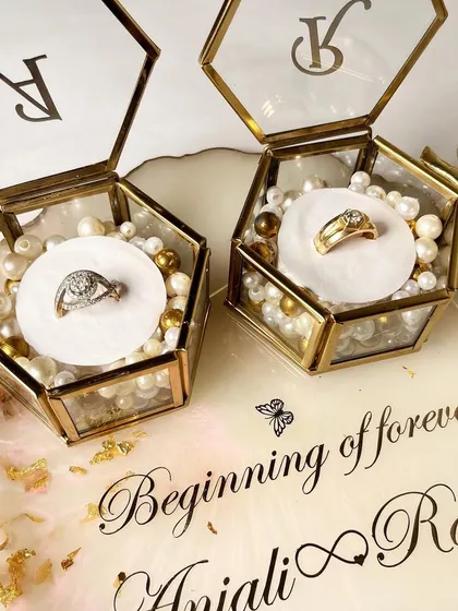 A close-up of the rings nestled in the hexagonal glass boxes on this classic white and gold tray. The boxes are filled with pearls and can be personalized with your initials.