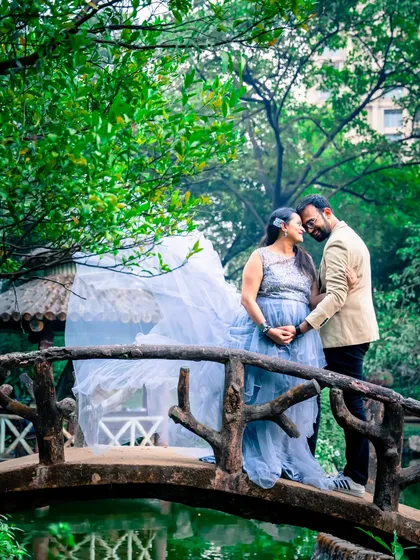 A romantic moment on a bridge over the water. The sheer fabric of the gown catches the light beautifully, adding to the dreamy atmosphere.