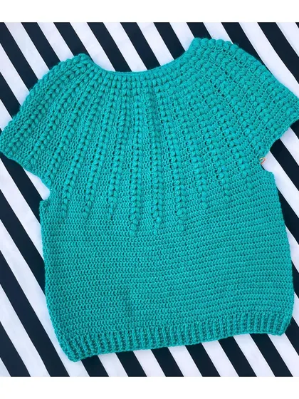 Here is the Goldenrod Sweater, a beautiful short-sleeved top made with soft cotton yarn. The textured stitch work gives it a lovely feel, and it's perfect for a casual day out. This piece is laid flat to show the full body construction before it's worn.