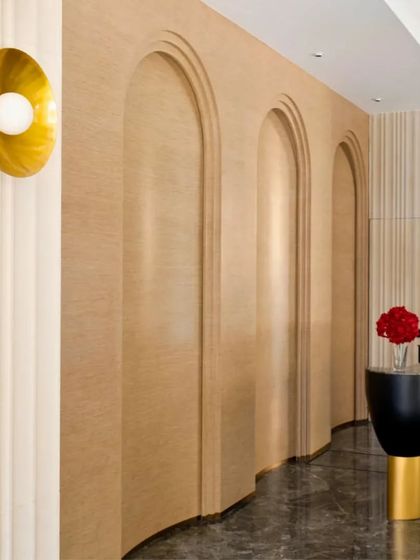 The curved wall with arched doorways, finished in a light wood texture, creates a soft and elegant corridor. A simple, gold wall sconce adds a touch of modern sophistication to the space.