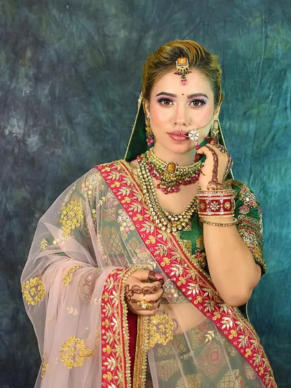 A portrait of a model in a traditional green and red bridal lehenga, showcasing the detailed henna and jewelry.