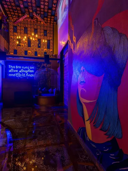 This moody, neon-lit corridor in one of our restobar projects sets the tone for a high-energy night. The combination of a bold mural and a "This bar runs on love, laughter, and cold beer" sign creates a fun and inviting atmosphere.