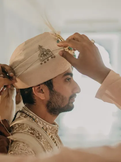 The groom's turban being adjusted, a traditional moment captured with artistic detail. It’s these small, significant rituals that add depth and meaning to the wedding celebration.