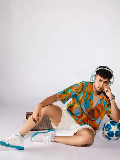 A relaxed, seated pose that shows off the full summer outfit, including the sneakers and football prop. It tells a story of a fun, active, and stylish guy.