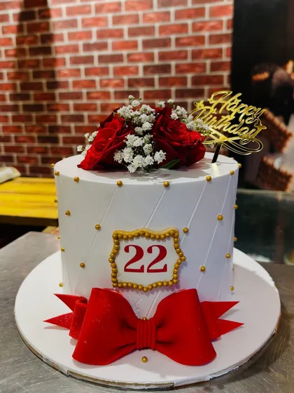 A chic white cake for a 22nd birthday, featuring a large red bow and fresh red roses.
