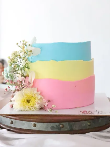 A fun and colorful cake with pastel layers of blue, yellow, and pink. The fresh flower accents make it a cheerful choice for a happy celebration.
