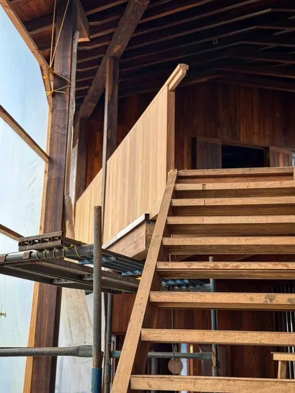 The interior of the farmhouse shows the intricate process of building the wooden structure. A temporary staircase provides access while the final handcrafted piece is being perfected.