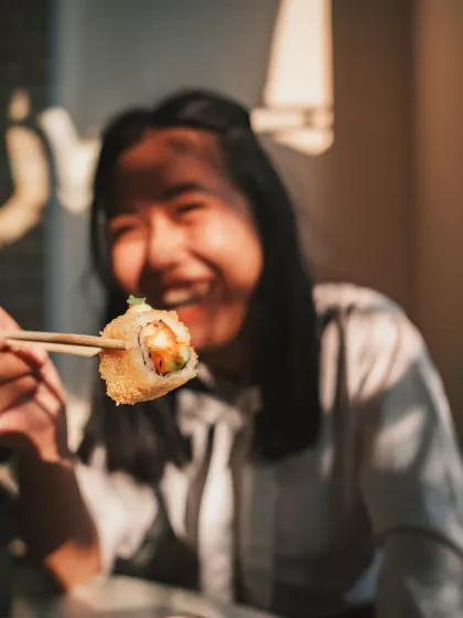 The pure joy of a perfect bite of sushi. A guest enjoys a crispy tempura roll, capturing the fun and flavor of our weekend menu.