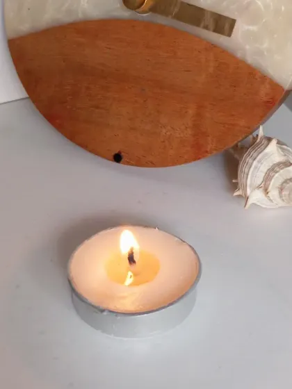 A lit tealight placed next to a clock and a seashell, showing how my candles can be a part of your everyday decor and moments of peace.
