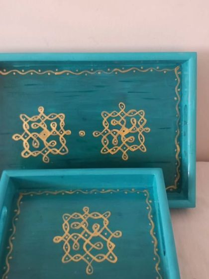 A set of two matching turquoise wooden trays with intricate Kolam designs painted in gold. These are perfect for gifting or for adding a touch of coordinated elegance to your home.