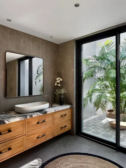 A wider view of the bathroom, showing the seamless connection to the outdoor courtyard through large sliding glass doors. The combination of natural wood, patterned tiles, and lush greenery creates a spa-like retreat.