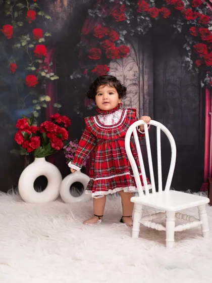 Standing tall and proud in a storybook setting. This full-length shot shows off her adorable red plaid dress against our enchanting rose-covered archway backdrop.