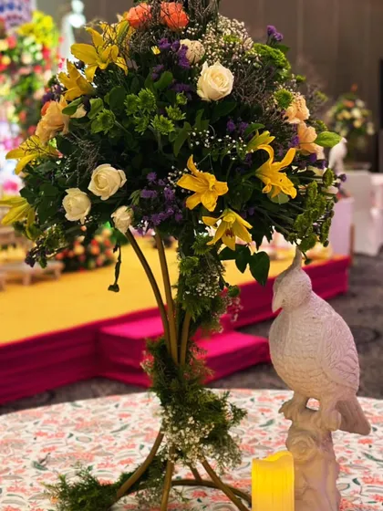 A rustic yet elegant centerpiece for a Mehendi brunch, featuring a tall floral arrangement and a whimsical bird statue.