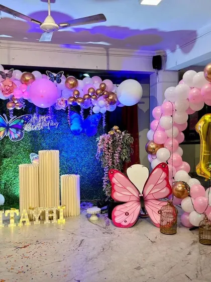 A beautiful butterfly-themed first birthday party. The combination of a grass wall backdrop, pink and gold balloons, and large butterfly props creates a whimsical and enchanting atmosphere.