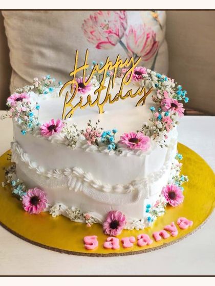 A lovely heart-shaped birthday cake adorned with fresh baby's breath flowers and a gold "Happy Birthday" topper.