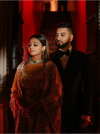 A stylish couple portrait from a sangeet and reception event at Mundota Palace. The dramatic red lighting and their elegant attire create a feeling of glamour and romance.