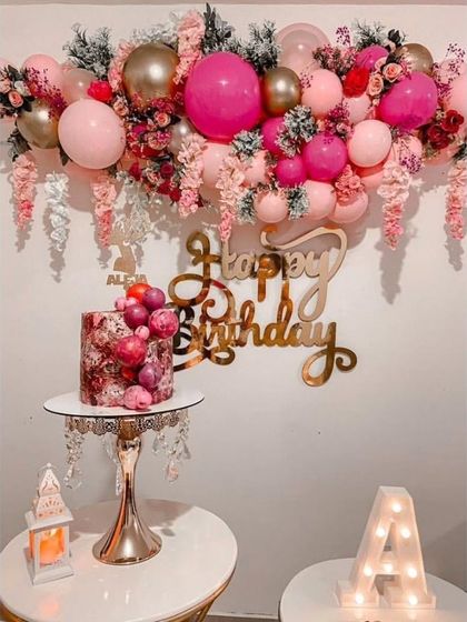 A stunning wall decoration with a balloon and flower garland in shades of pink, perfect for a cake-cutting ceremony.