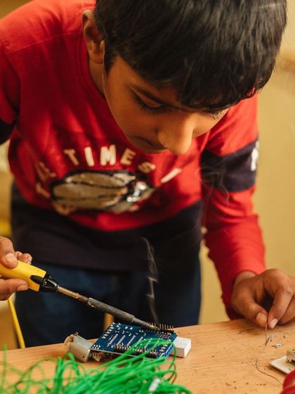 Safety and skill go hand in hand. Here, a student learns how to properly use a soldering iron to connect components on a circuit board under careful supervision.